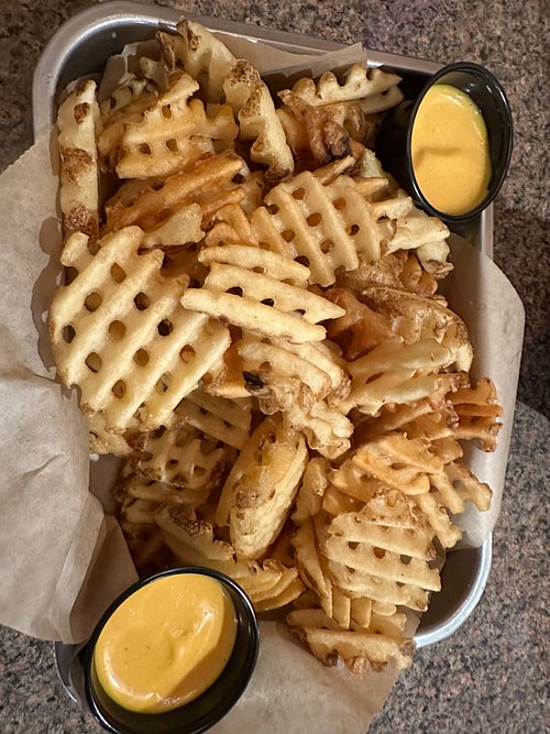 Basket of waffle fries with two cups of cheese sauce
